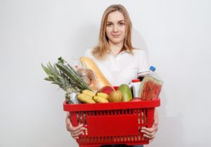 A woman holding a red shopping basket full of food.