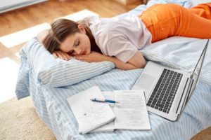 student lying in bed surrounded by notes and laptop