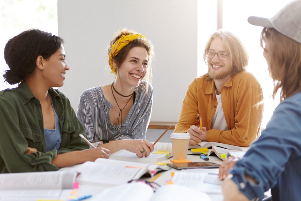 Four friendly students sitting in white classroom reading together