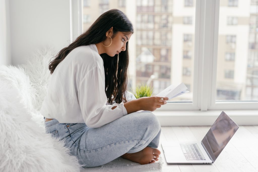 female university student sitting on bed with laptop and notebook using bionic reading