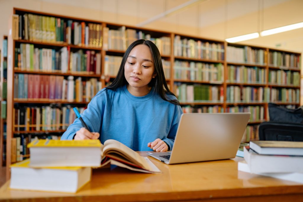 female student in library with books open on desk implementing university study skills