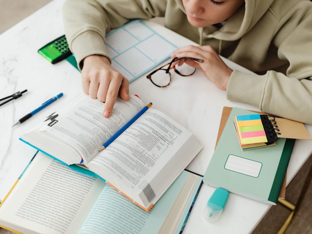 girl sat at a desk reading a book with notes all around her on the desk