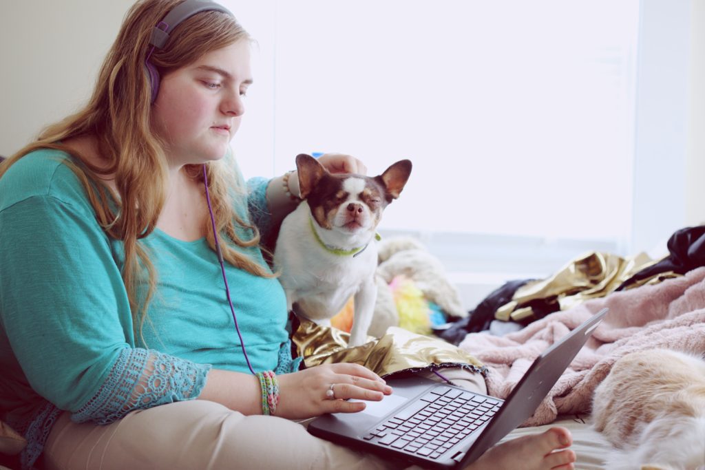 a student on a laptop with her dog whilst listening to music