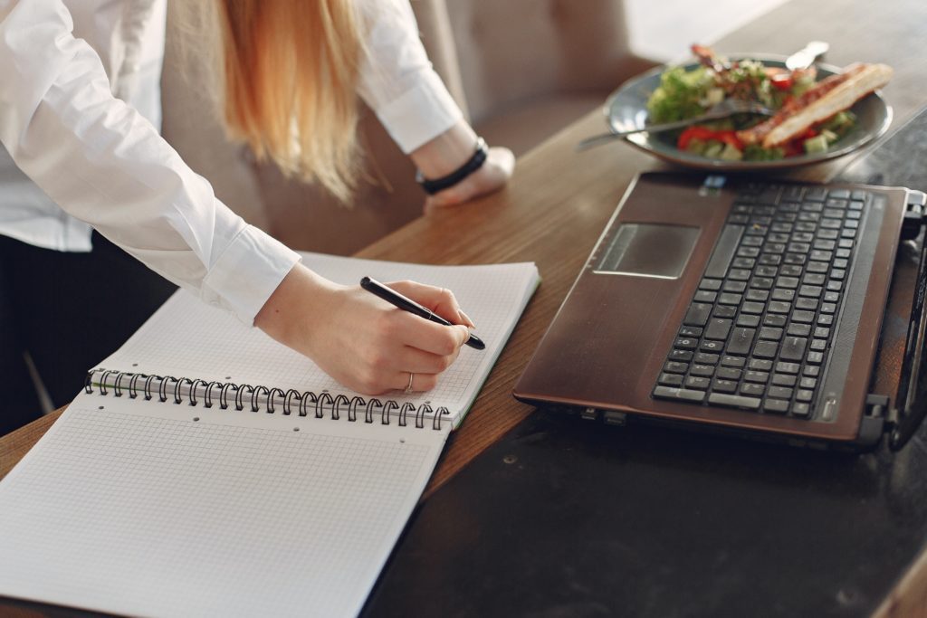 mature student taking notes at desk with open laptop