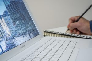 open laptop and notebook on desk with hand writing notes 