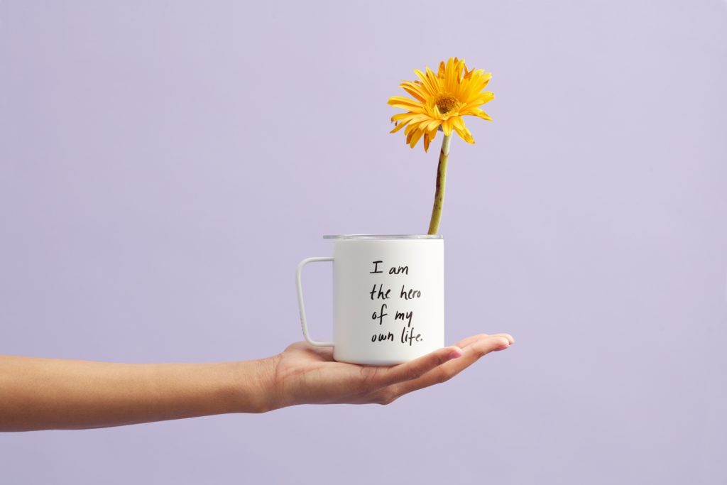 hand holding mug with positive affirmation for anxiety printed on side and flower standing inside