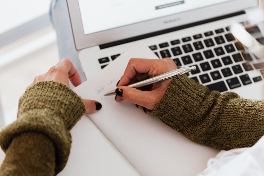 hands taking notes using notebook and laptop