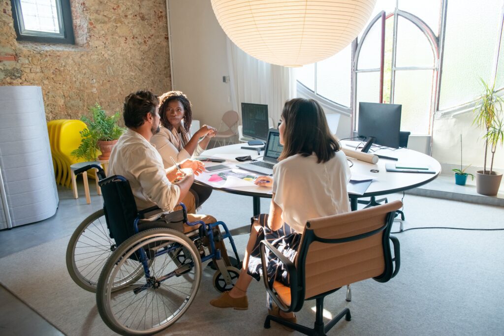 two females and a male in a wheelchar sitting at a desk with papers and devices