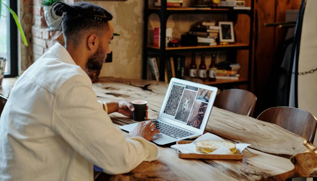 a man is seated at a table with an open laptop displaying images on the screen