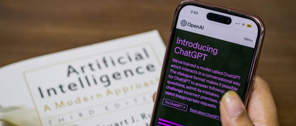 image of a hand holding smart phone with chatgpt open and ai textbook in the background