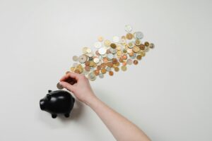 Pennies falling out of a Piggy bank with a human hand picking them up.